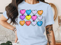 A person wears a light blue t-shirt featuring a graphic of twelve colorful conversation hearts.