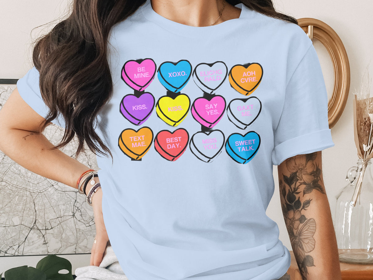 A person wears a light blue t-shirt featuring a graphic of twelve colorful conversation hearts.