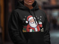A person wearing a black hooded sweatshirt with a graphic of Santa Claus surrounded by gifts.
