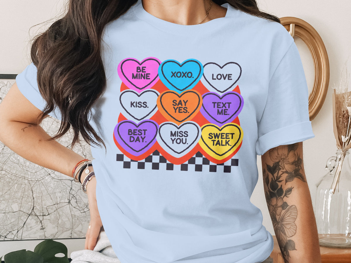 Light blue t-shirt with a graphic of conversation hearts featuring text like "BE MINE", "XOXO", and "LOVE".