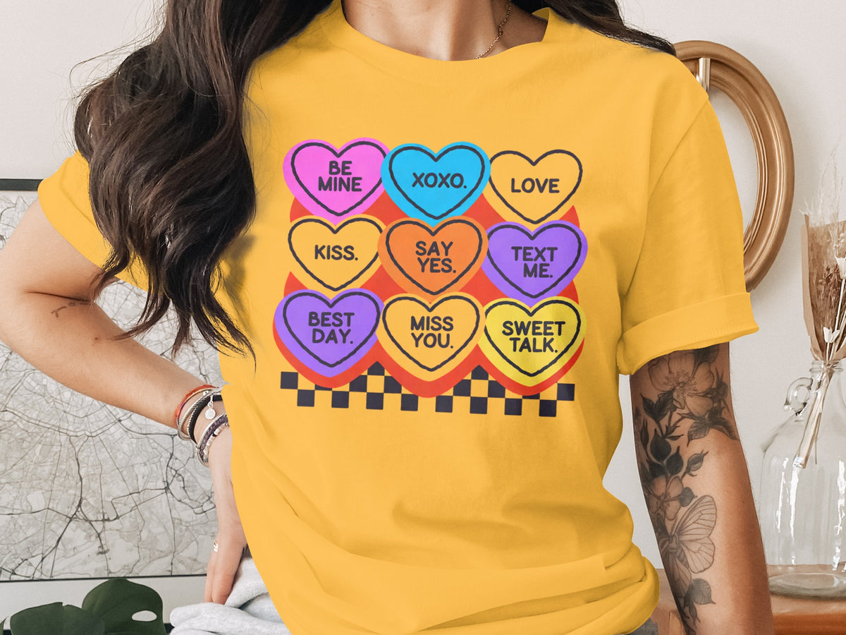 A woman wears a yellow t-shirt featuring a graphic of colorful candy hearts with text.