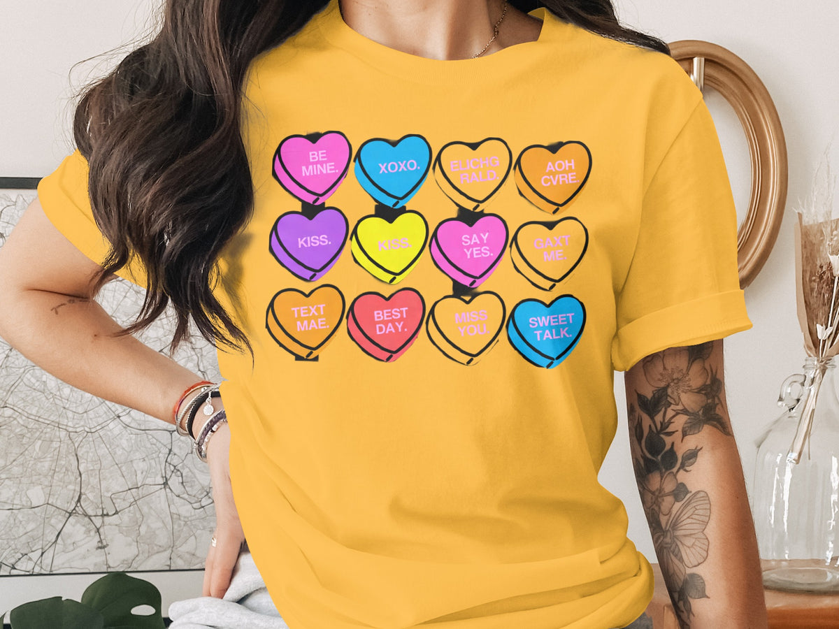 A person wearing a bright yellow t-shirt featuring a graphic of twelve colorful candy hearts with text.