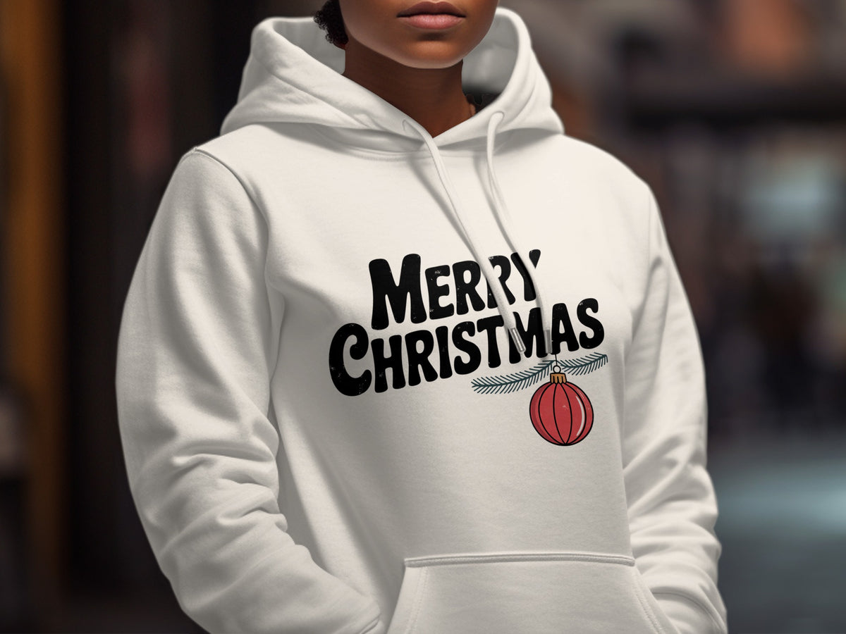 A person wearing a white hooded sweatshirt printed with black text reading MERRY CHRISTMAS and a red ornament.