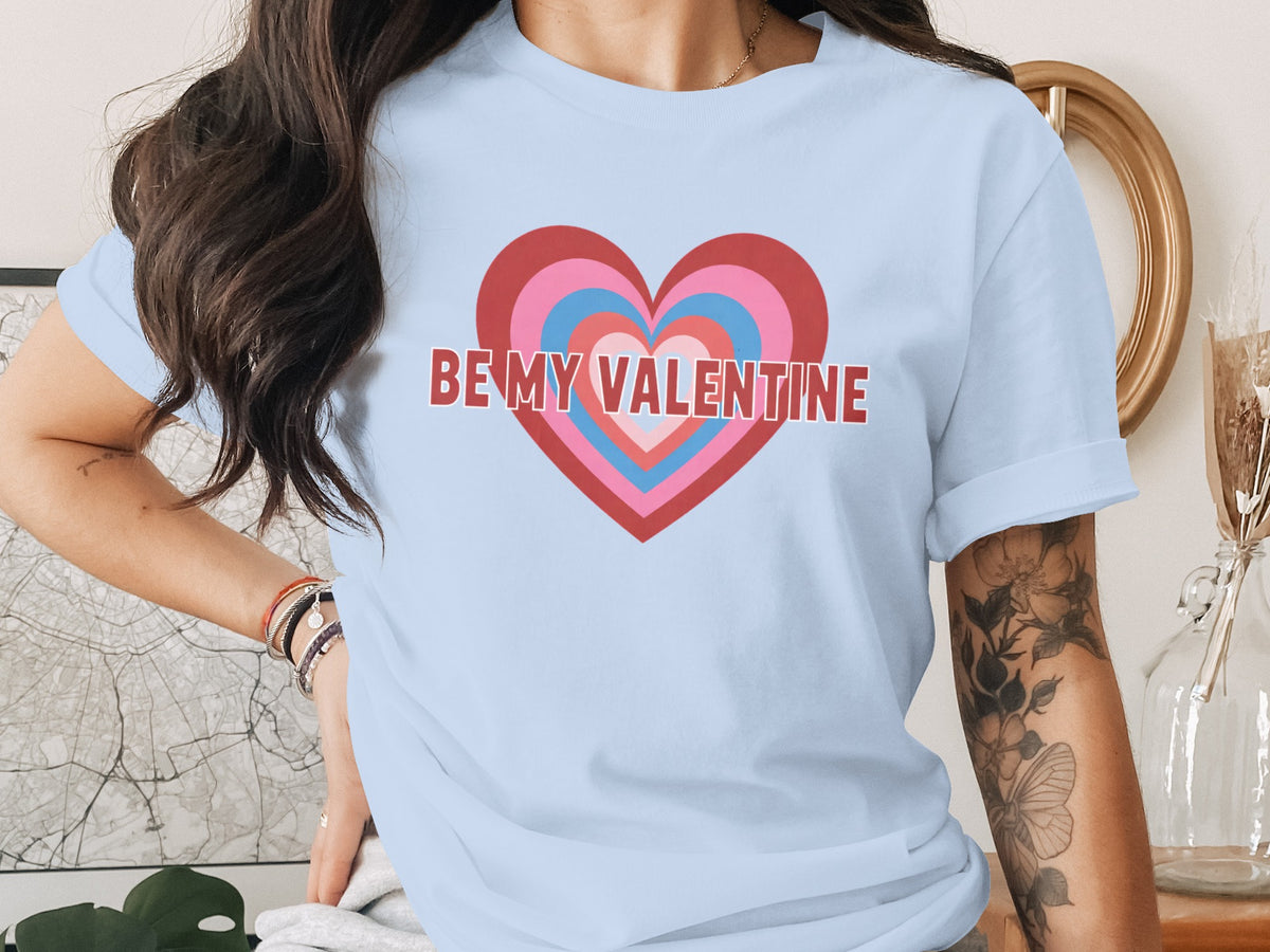 A person wearing a light blue t-shirt featuring concentric hearts and the text Be My Valentine.