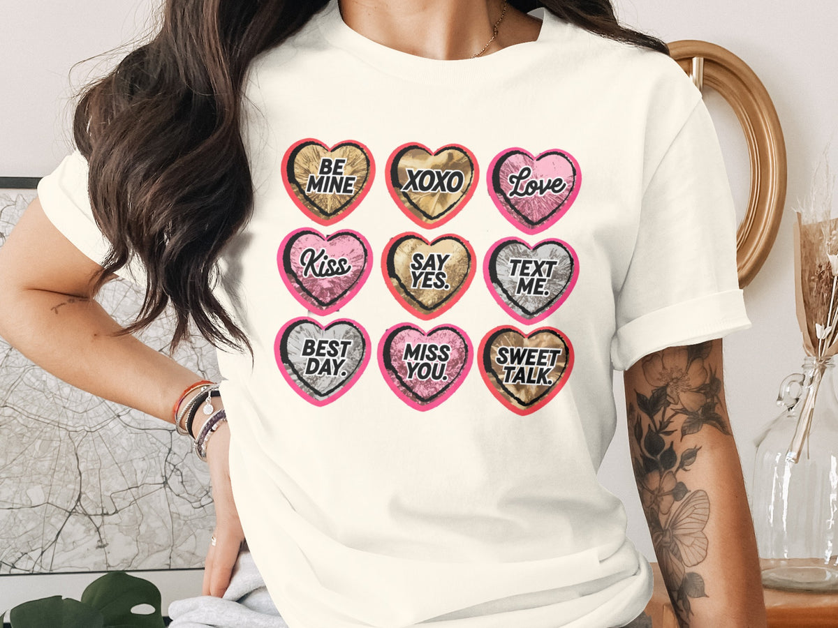 A person wearing a white t-shirt featuring a grid of nine Valentine's candy hearts with phrases.