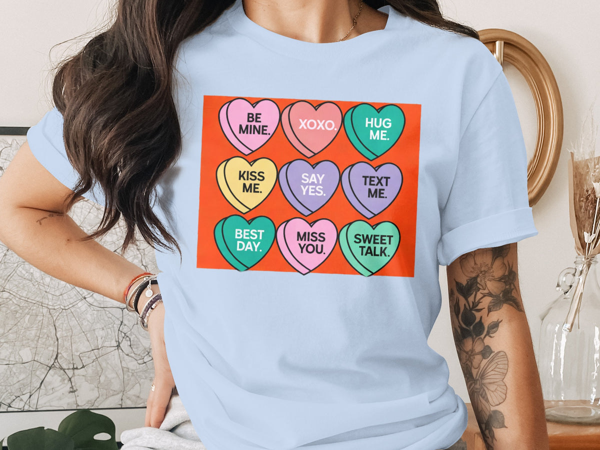 Light blue t-shirt featuring a graphic of nine colorful candy hearts with text on an orange background.