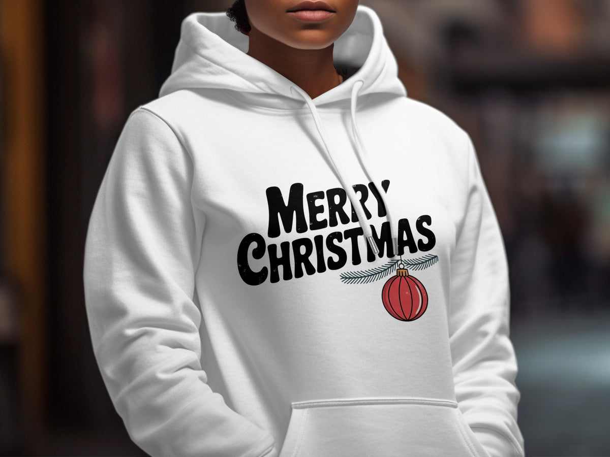 A person wearing a white hooded sweatshirt with bold black text reading Merry Christmas and a hanging red ornament.