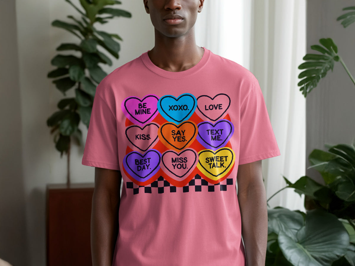 A man wearing a pink t-shirt with a graphic of colorful candy hearts containing various messages.