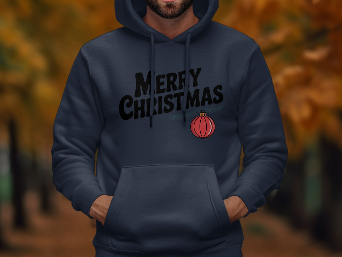 A person wearing a dark blue hooded sweatshirt featuring black text reading "MERRY CHRISTMAS" and a red ornament.