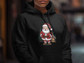 A person wearing a black hoodie with a graphic print of Santa Claus in front of trees.