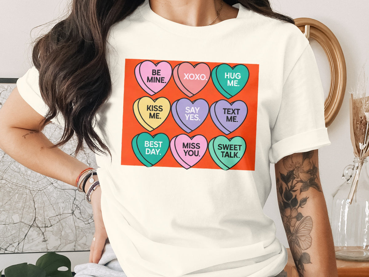 A woman wearing a white t-shirt featuring a graphic of nine colorful candy hearts with text.