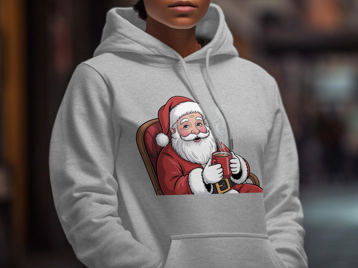A person wearing a light gray hoodie printed with a cartoon graphic of Santa Claus drinking hot cocoa.