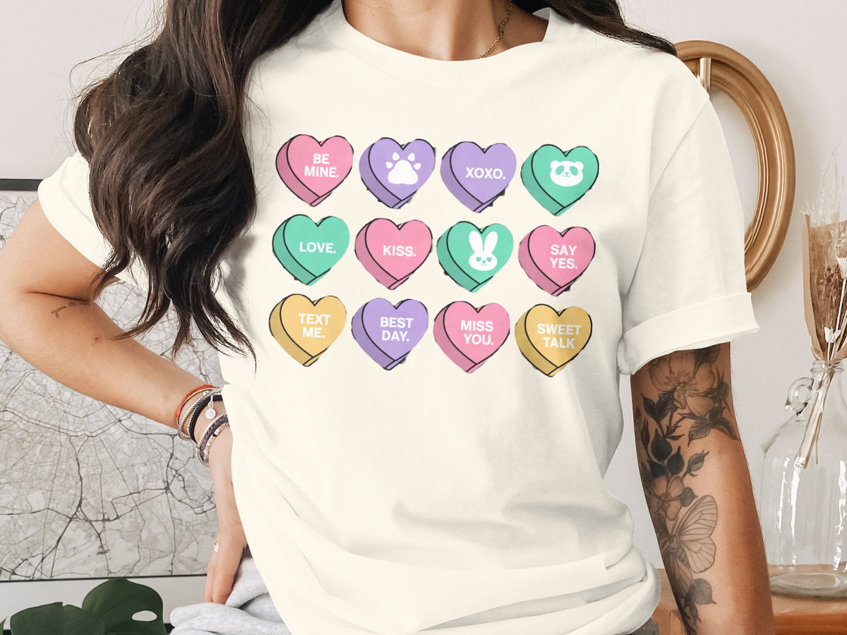 A person wearing an off-white t-shirt printed with a grid of twelve colorful conversation hearts.