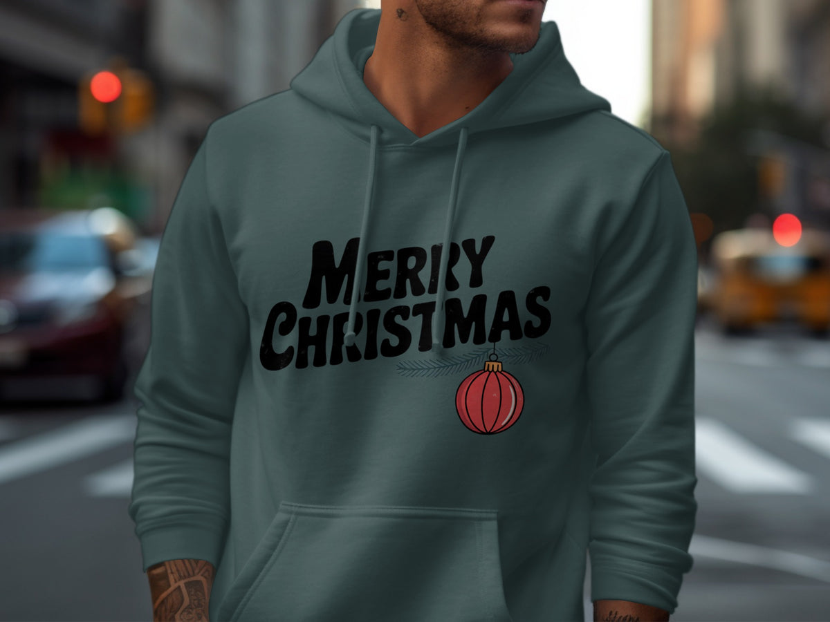 A man wearing a grey hoodie featuring black text that reads Merry Christmas alongside a hanging red ornament.