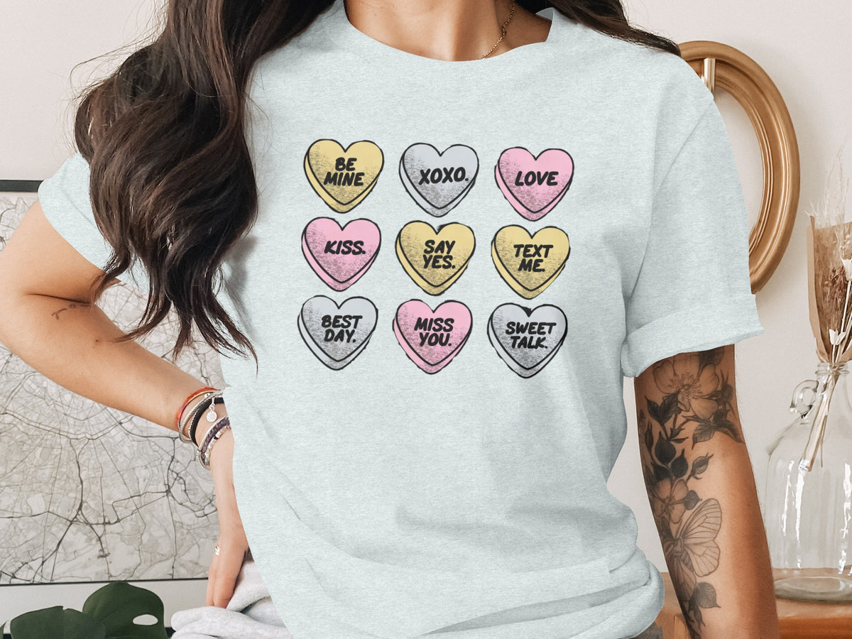 A light grey crewneck t-shirt featuring a graphic of nine pastel conversation hearts with romantic text.