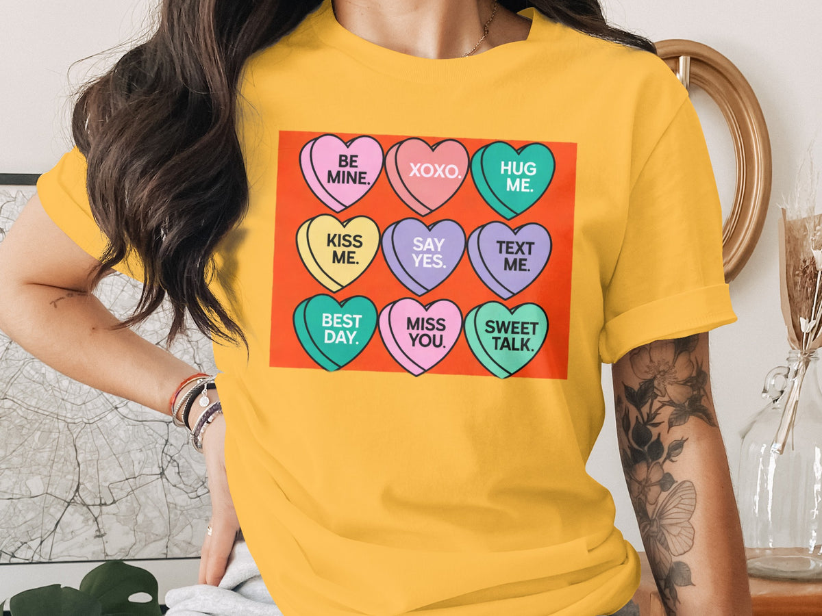 Yellow t-shirt with nine candy hearts featuring messages like "Be Mine" and "XOXO".