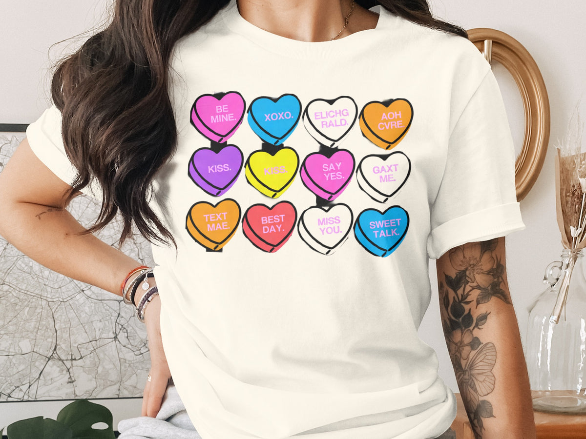 A person wearing an off-white t-shirt printed with a grid of colorful conversation hearts.