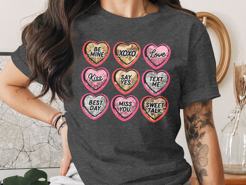 A dark gray t-shirt featuring a grid of nine colorful hearts printed with romantic messages.