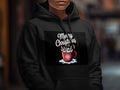 A person wears a black hoodie printed with a red mug graphic and the text Merry Christmas.