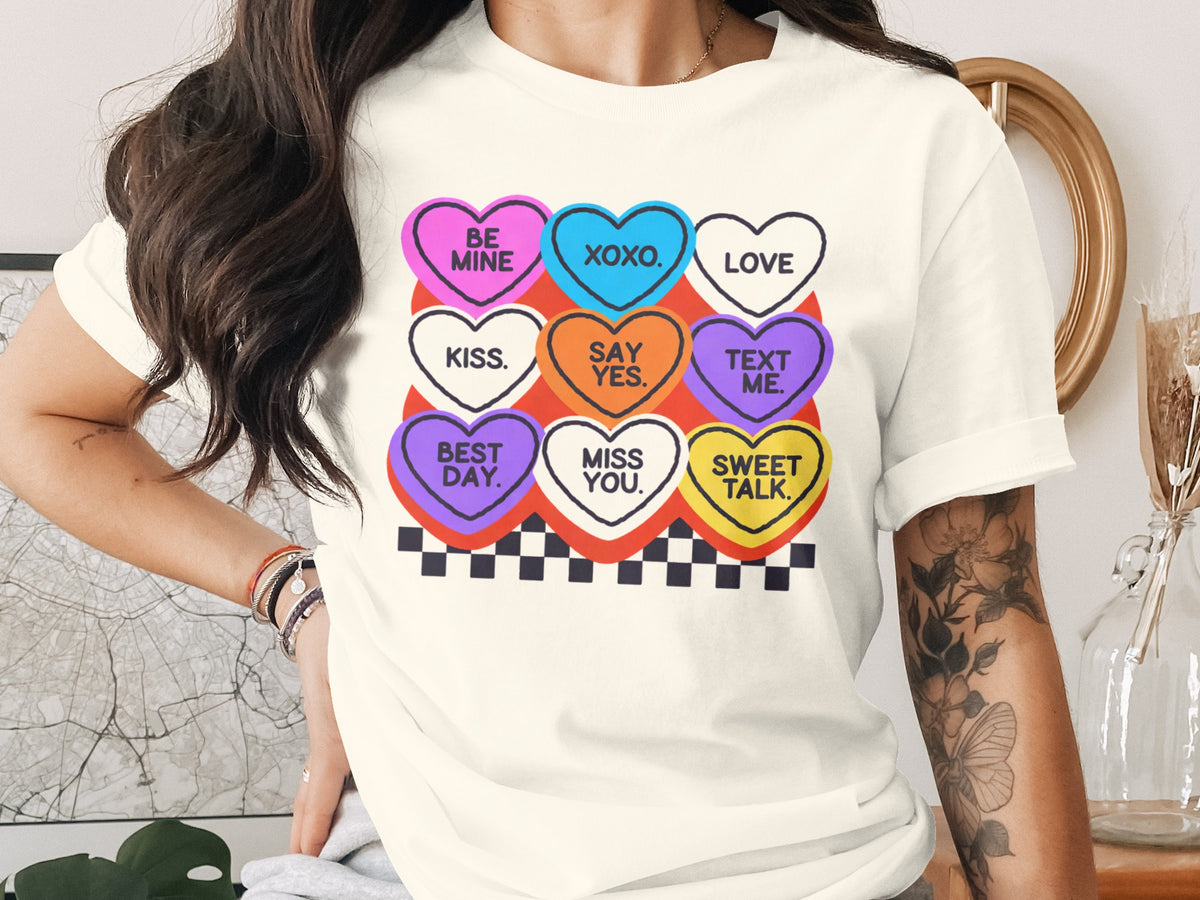 Cream t-shirt with nine conversation heart graphics featuring Valentine's Day phrases.