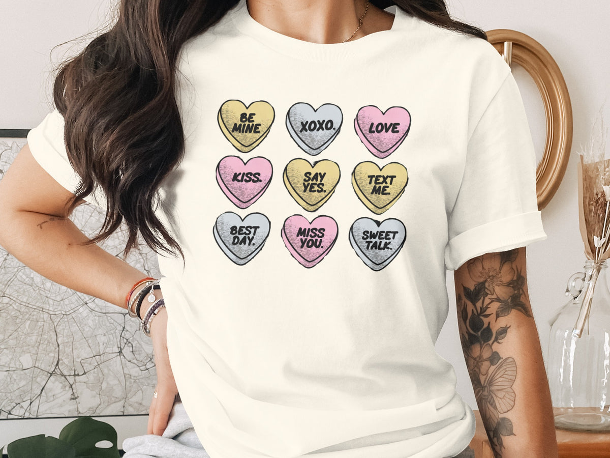 Cream t-shirt with nine conversation hearts saying "BE MINE", "XOXO.", "LOVE", "KISS.", "SAY YES.", "TEXT ME.", "BEST DAY.", "MISS YOU.", and "SWEET TALK.".