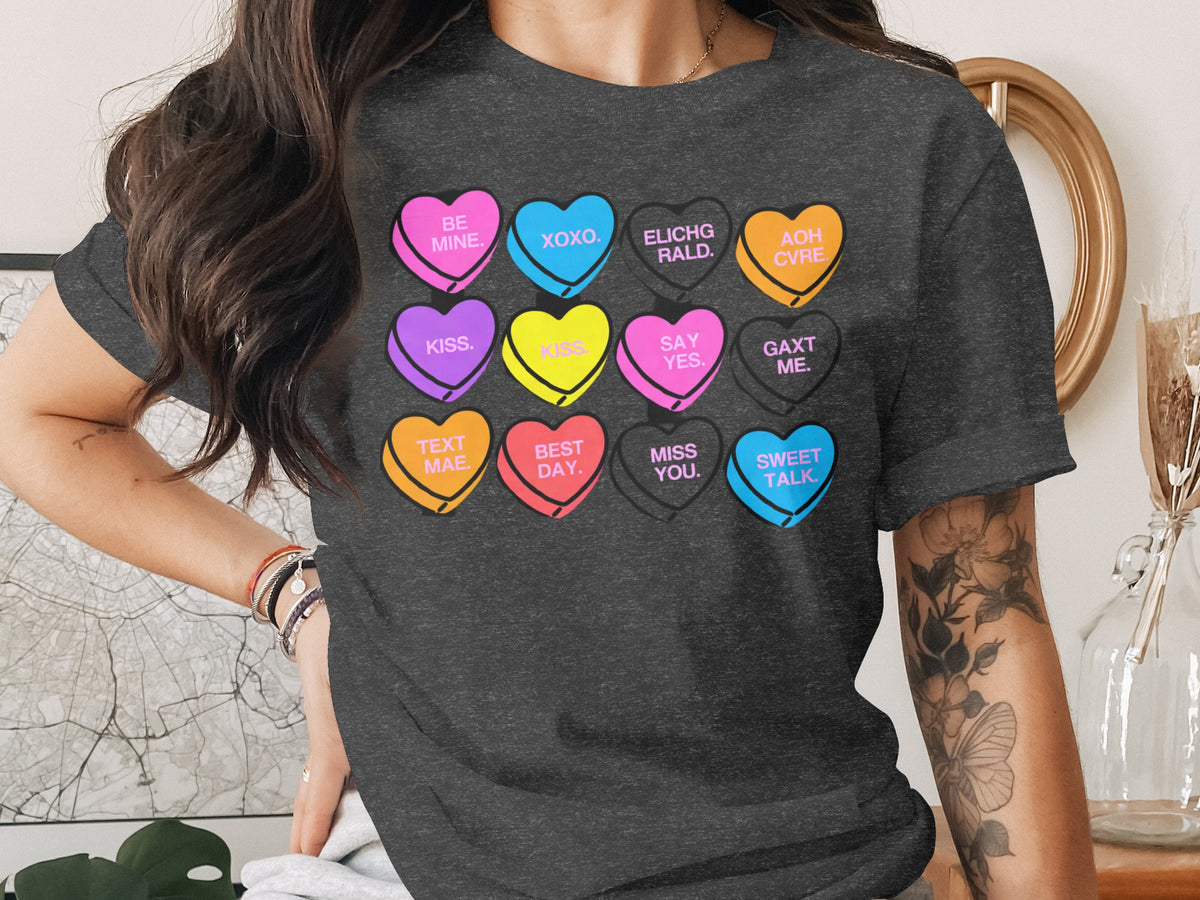A woman wearing a dark gray t-shirt printed with a grid of colorful, conversation heart candies with text.